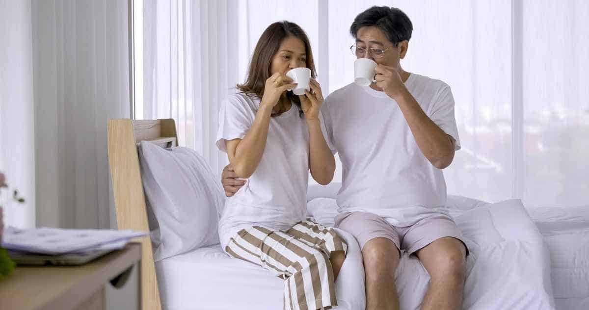 Happy asian couple drinking coffee together in bedroom.